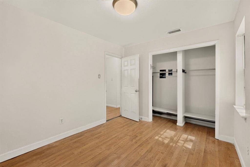 Wood-finish flooring, recessed closet storage, white trim, and a ceiling-mounted light fixture