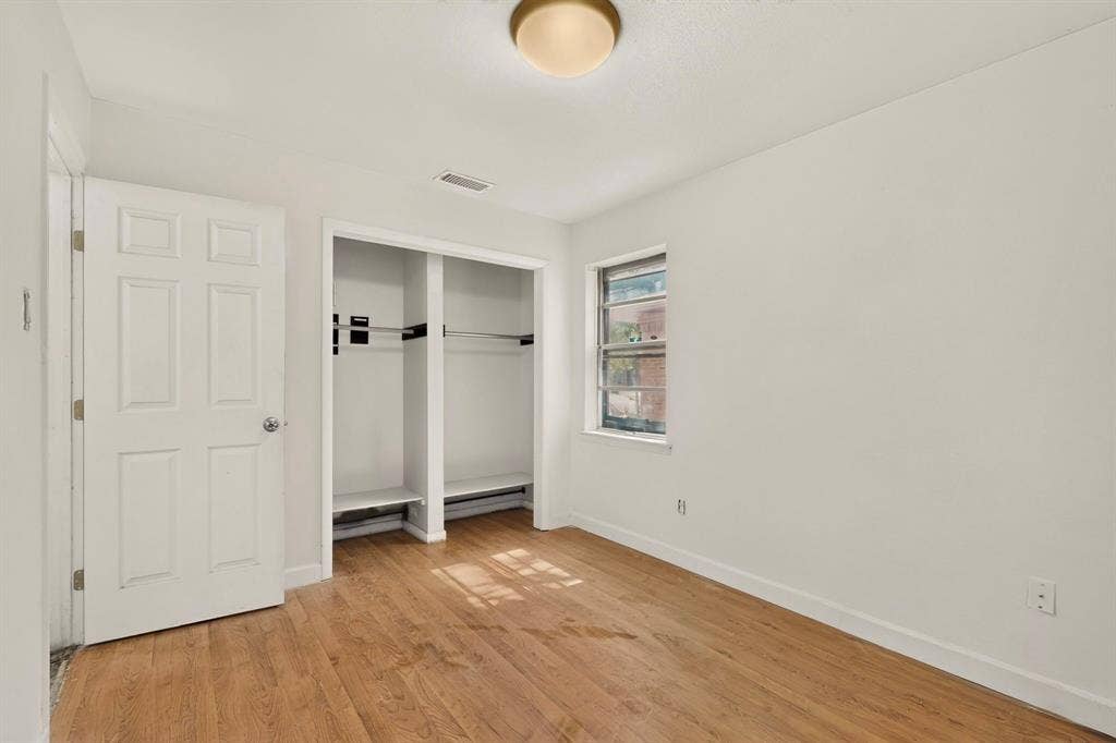Wood-finish flooring, white walls, built-in closet storage, window with exterior light, and a ceiling-mounted light fixture