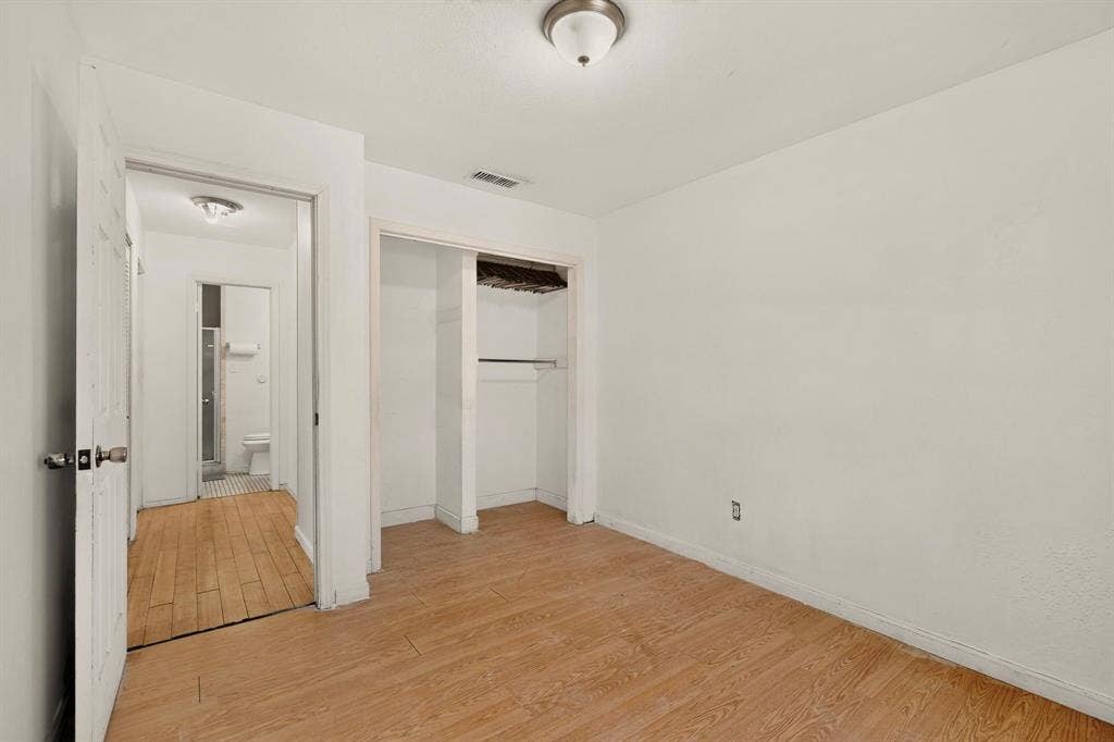 Wood-finish flooring, recessed closet with shelving, overhead flush-mount lighting, and white interior doors