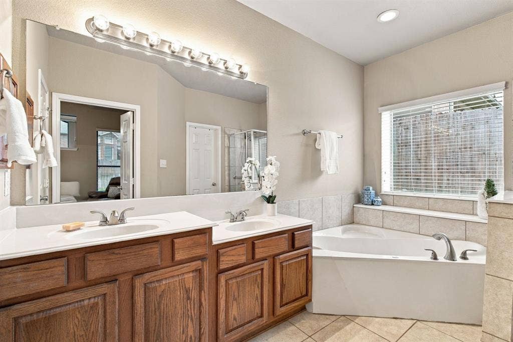 4220 Boxwood Drive, Denton, TX 76208 Dual vanity with integrated sinks, wood-finish cabinetry, built-in soaking tub, tile surround, and tile flooring