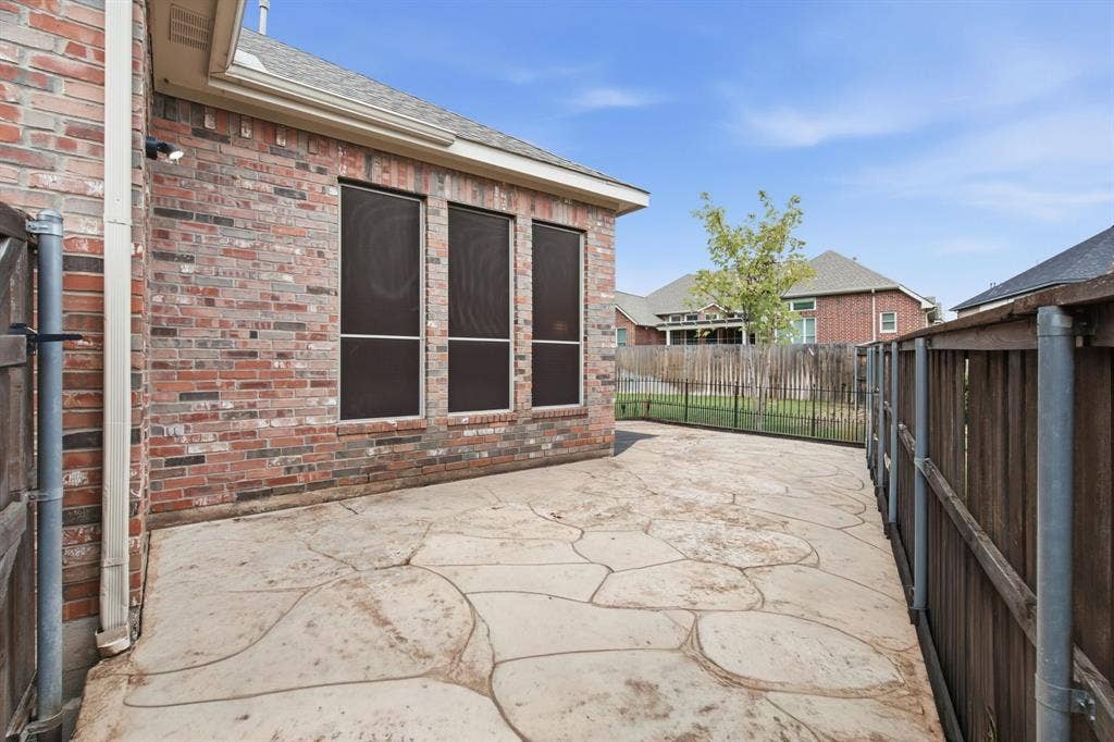 4220 Boxwood Drive, Denton, TX 76208 Stained concrete patio with a brick exterior, three windows with solar screens, and a wood privacy fence