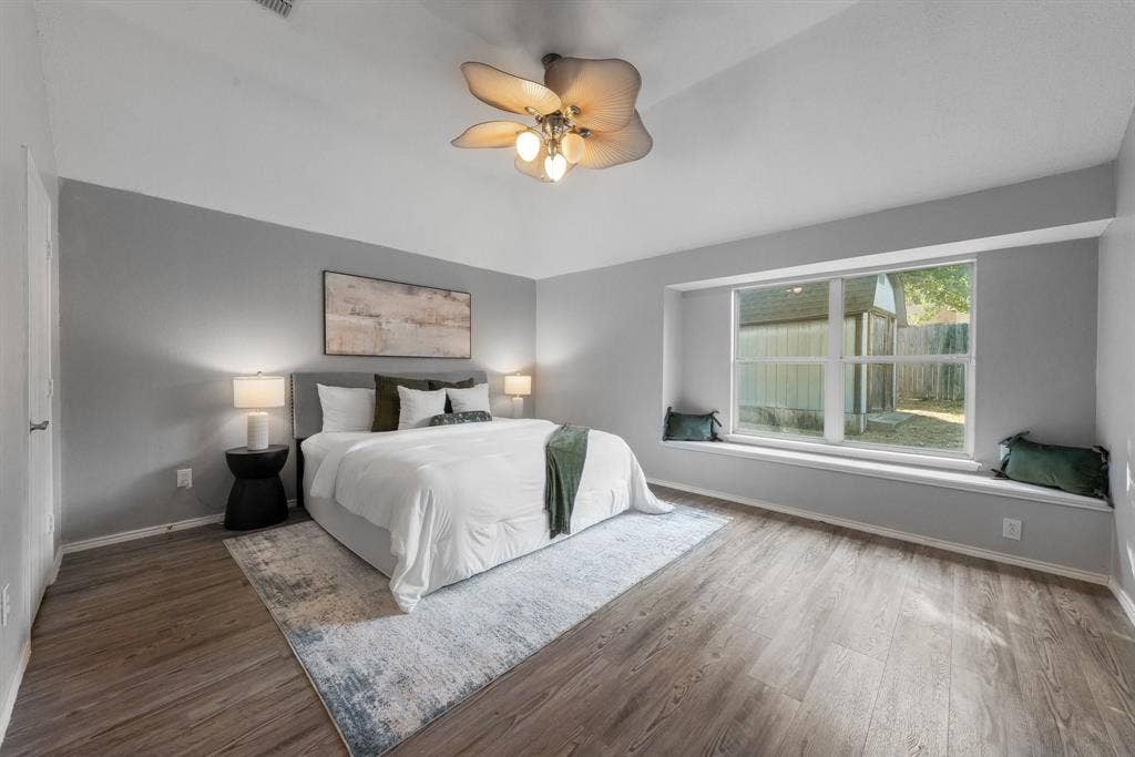 215 Longhorn Trail, Grand Prairie, TX 75052 Spacious primary bedroom featuring wood-finish flooring, soft gray walls, and abundant natural light from large multi-pane windows