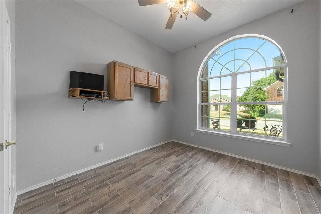 215 Longhorn Trail, Grand Prairie, TX 75052 Arch-top window with decorative grid, light wood-finish flooring, ceiling fan with integrated lighting, and built-in wood cabinetry