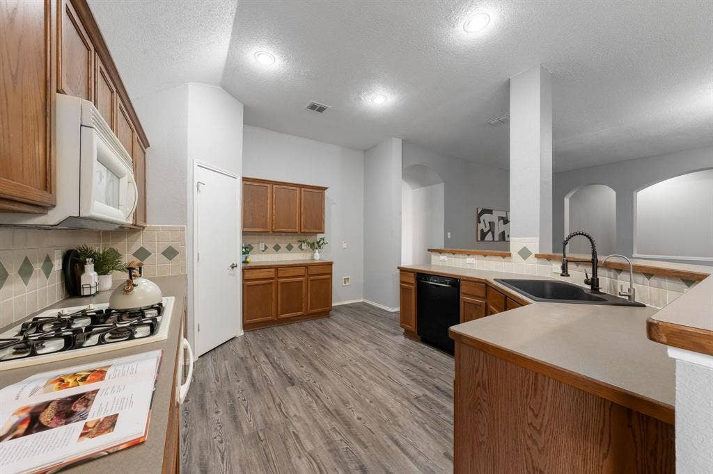 215 Longhorn Trail, Grand Prairie, TX 75052 Kitchen featuring extensive wood cabinetry, wood-finish flooring, a black sink with a matte black faucet, and a gas range