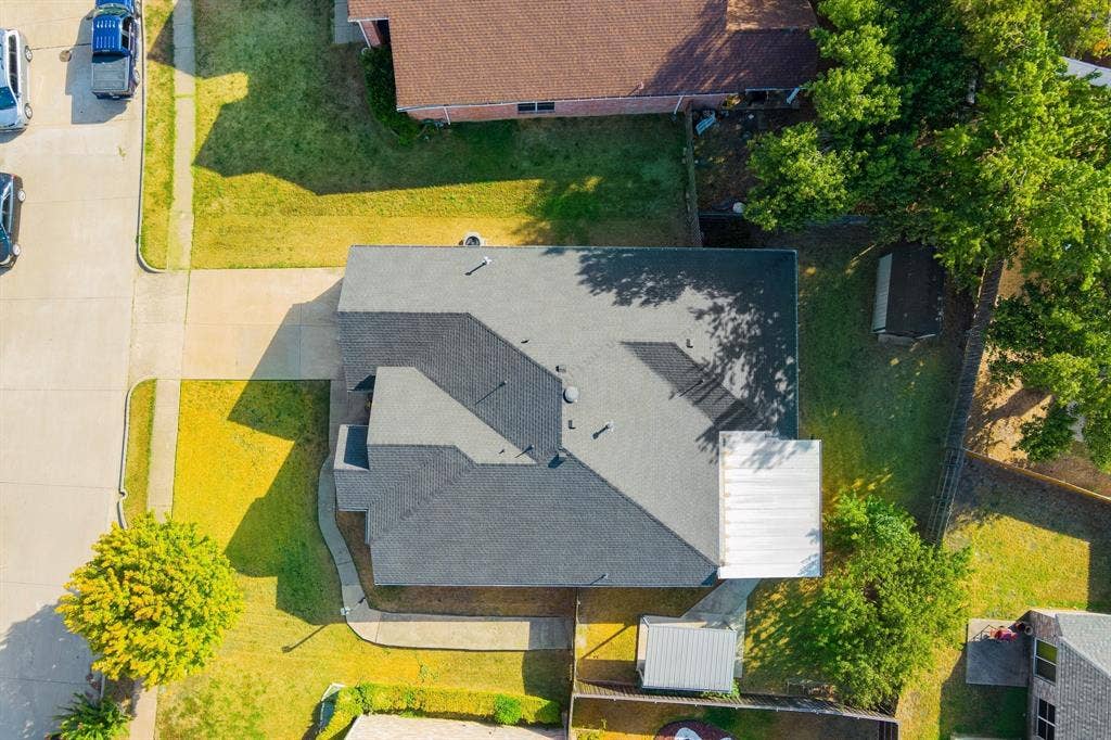 215 Longhorn Trail, Grand Prairie, TX 75052 Expansive lot featuring a concrete driveway, established trees, and a gray shingled roof