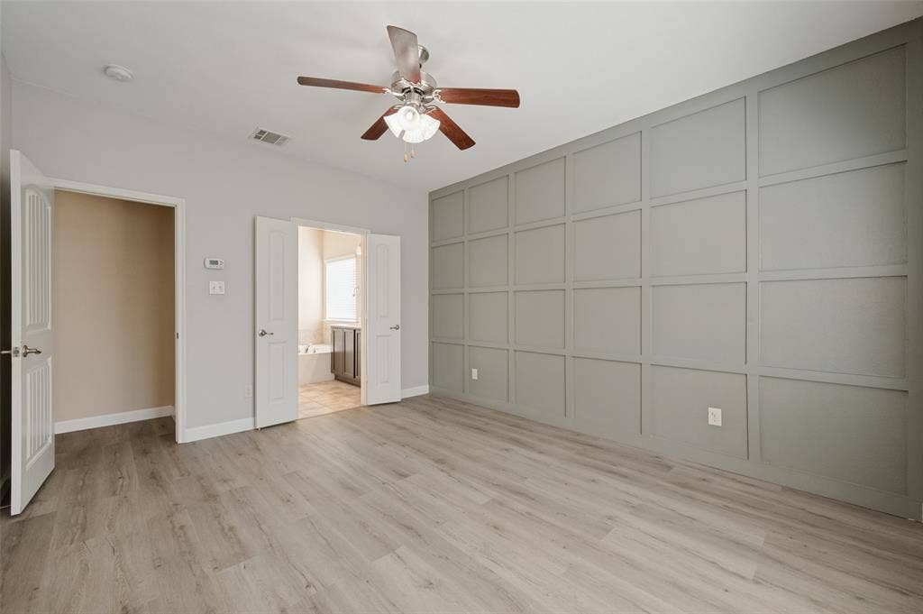 9801 Moccasin Creek Lane, McKinney, TX 75071 Wood-finish flooring, accent wall with panel detailing, ceiling fan with light fixture, double doors, and a built-in bathtub