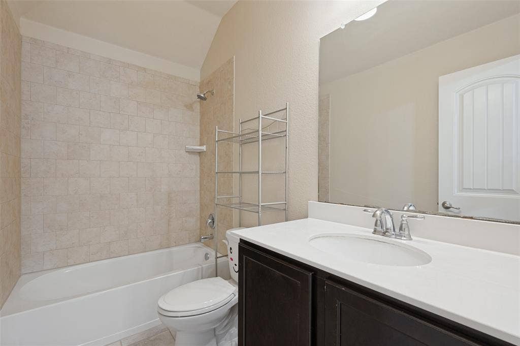 9801 Moccasin Creek Lane, McKinney, TX 75071 Bathroom featuring a white bathtub, tiled shower surround, dark wood-finish vanity with an integrated sink, and a large wall-mounted mirror