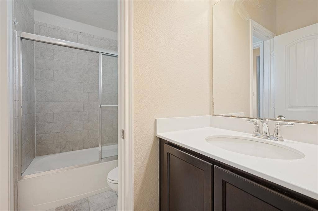 9801 Moccasin Creek Lane, McKinney, TX 75071 Bathroom featuring a dark wood-finish vanity with an integrated white sink, chrome faucet, and a large mirror