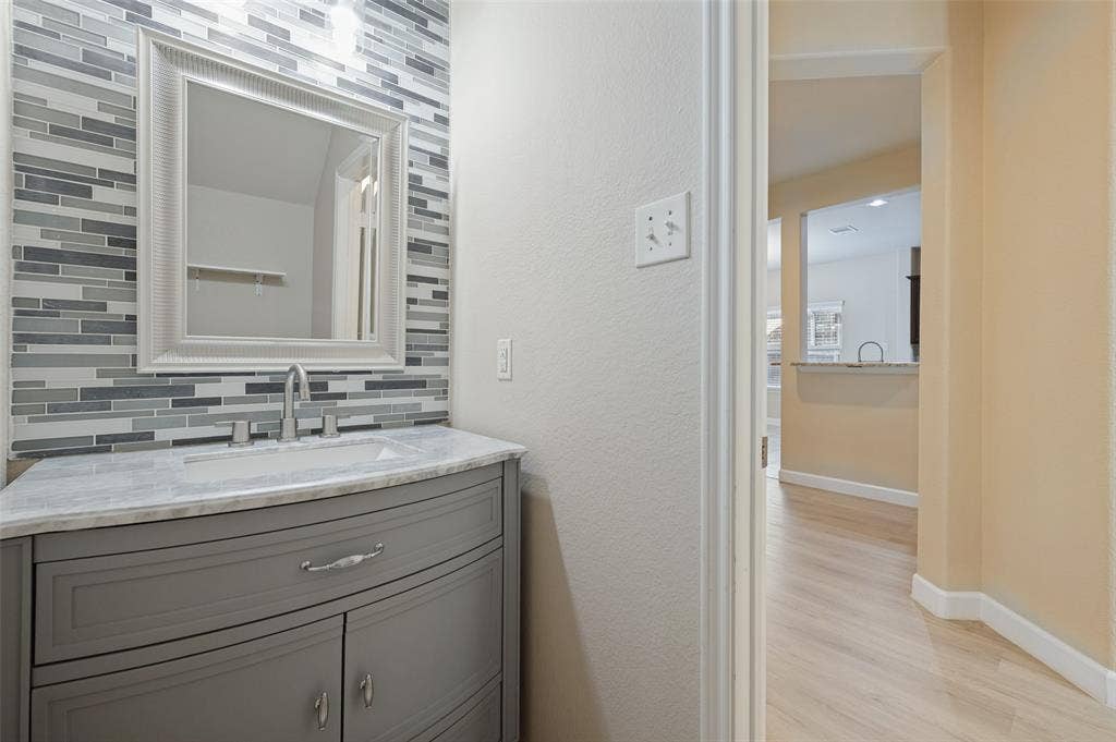 9801 Moccasin Creek Lane, McKinney, TX 75071 Vanity with gray cabinet and integrated sink, marble-finish countertop, and decorative tile backsplash