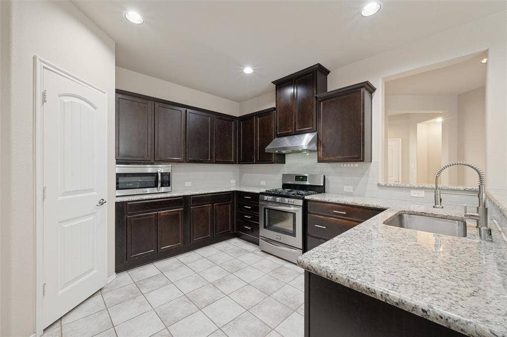 9801 Moccasin Creek Lane, McKinney, TX 75071 Kitchen featuring dark wood cabinetry, light-colored granite countertops, and stainless steel appliances including a range and microwave