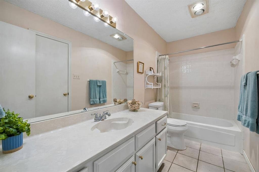 1902 Wyatt Drive, Garland, TX 75040 Bright, spa-like bathroom featuring a double vanity with white quartz countertop, polished chrome fixtures, and abundant mirror lighting