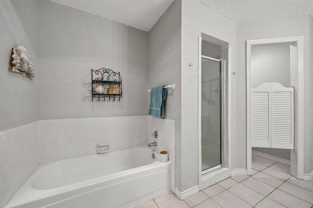 1902 Wyatt Drive, Garland, TX 75040 White tiled flooring with a white bathtub and shower with glass enclosure