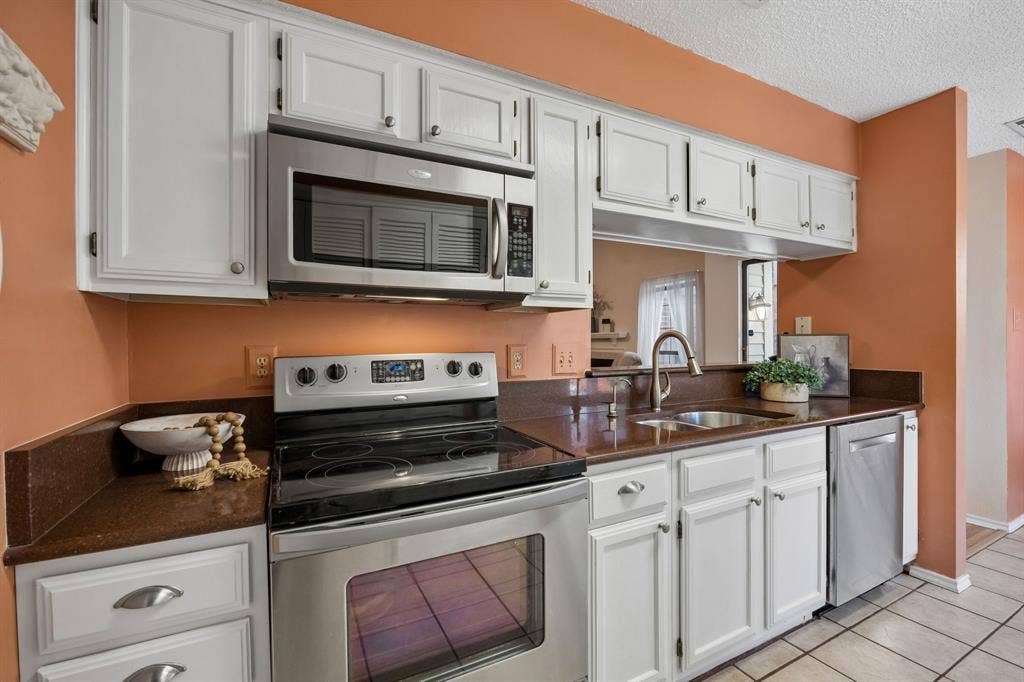1902 Wyatt Drive, Garland, TX 75040 White cabinetry, stainless steel appliances, dark countertops, and a stainless steel sink with a gooseneck faucet