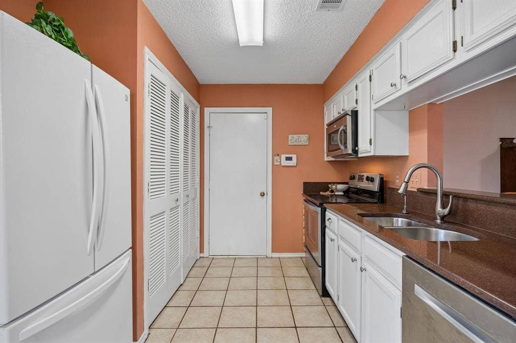 1902 Wyatt Drive, Garland, TX 75040 Galley kitchen featuring white cabinetry, stainless steel appliances, and a stainless steel sink with chrome faucet