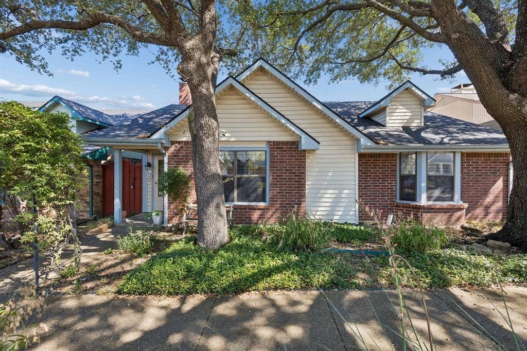 1902 Wyatt Drive, Garland, TX 75040 Charming brick residence featuring a classic gabled roofline, cream and brick exterior, and mature shade trees providing natural landscaping