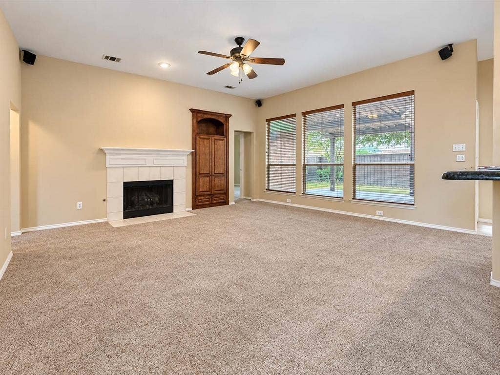 2504 Indian Paint Drive, Plano, TX 75025 Living space featuring a tiled fireplace with a white mantel, built-in wood cabinetry, a ceiling fan, recessed lighting, and three large windows