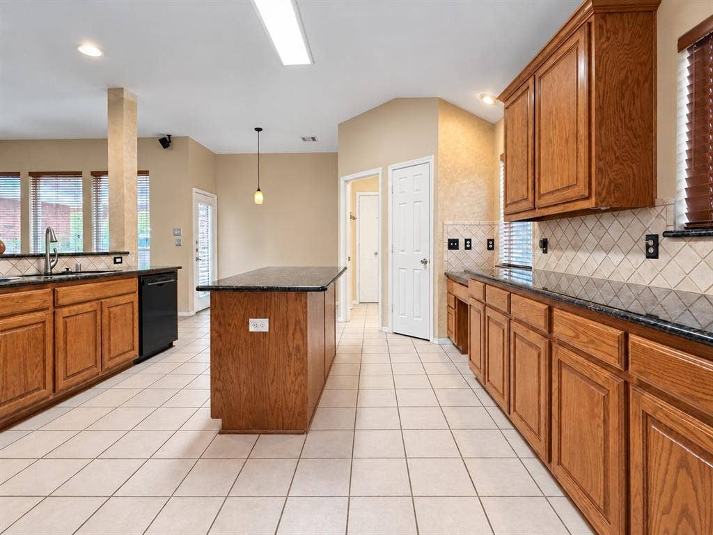 2504 Indian Paint Drive, Plano, TX 75025 Kitchen featuring wood cabinetry, dark countertops, a central island, tile flooring, and a tile backsplash