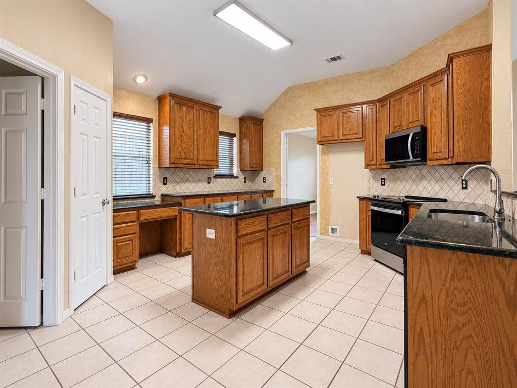 2504 Indian Paint Drive, Plano, TX 75025 Kitchen featuring wood cabinetry, dark countertops, a central island, stainless steel appliances, and a tiled backsplash