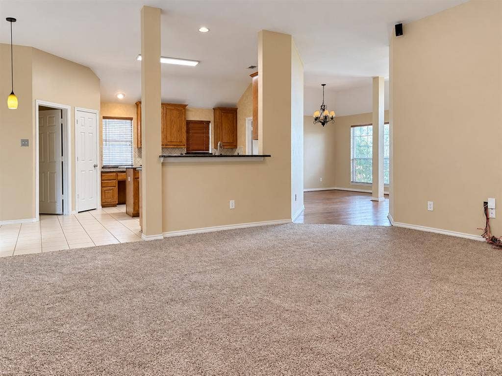 2504 Indian Paint Drive, Plano, TX 75025 Carpeted living area with vaulted ceilings, featuring an integrated kitchen with wood cabinetry and tile flooring, and a separate dining area with wood-finish flooring and a chandelier