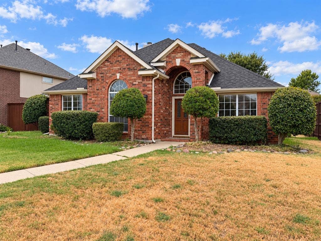 2504 Indian Paint Drive, Plano, TX 75025 Red brick exterior with white trim, arched window above the entry, dark shingle roof, and mature front landscaping