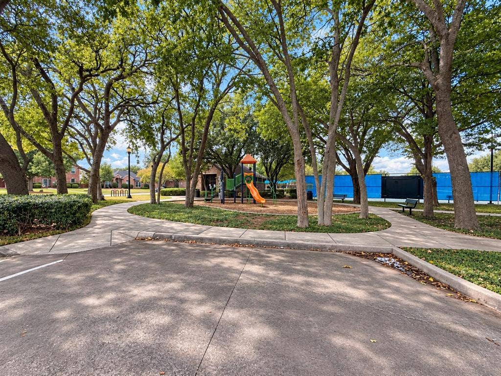 2504 Indian Paint Drive, Plano, TX 75025 Paved walkways surrounded by mature trees and manicured landscaping, featuring a playground and a tennis court with blue fencing