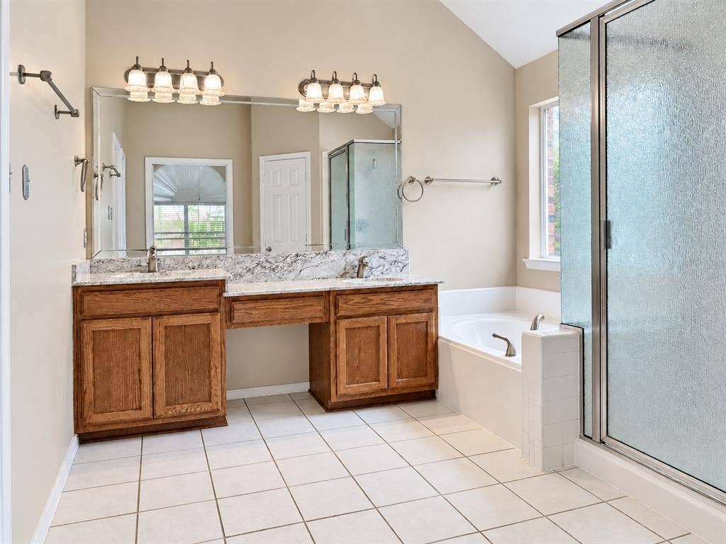 2504 Indian Paint Drive, Plano, TX 75025 Dual wood-finish vanities with light stone countertops, integrated soaking tub, and a glass-enclosed shower