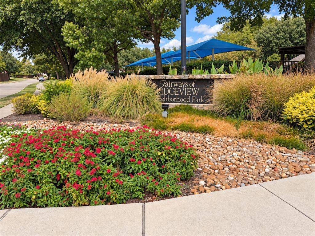 2504 Indian Paint Drive, Plano, TX 75025 Stone-clad neighborhood park sign, mature trees, vibrant red flowering shrubs, and ornamental grasses