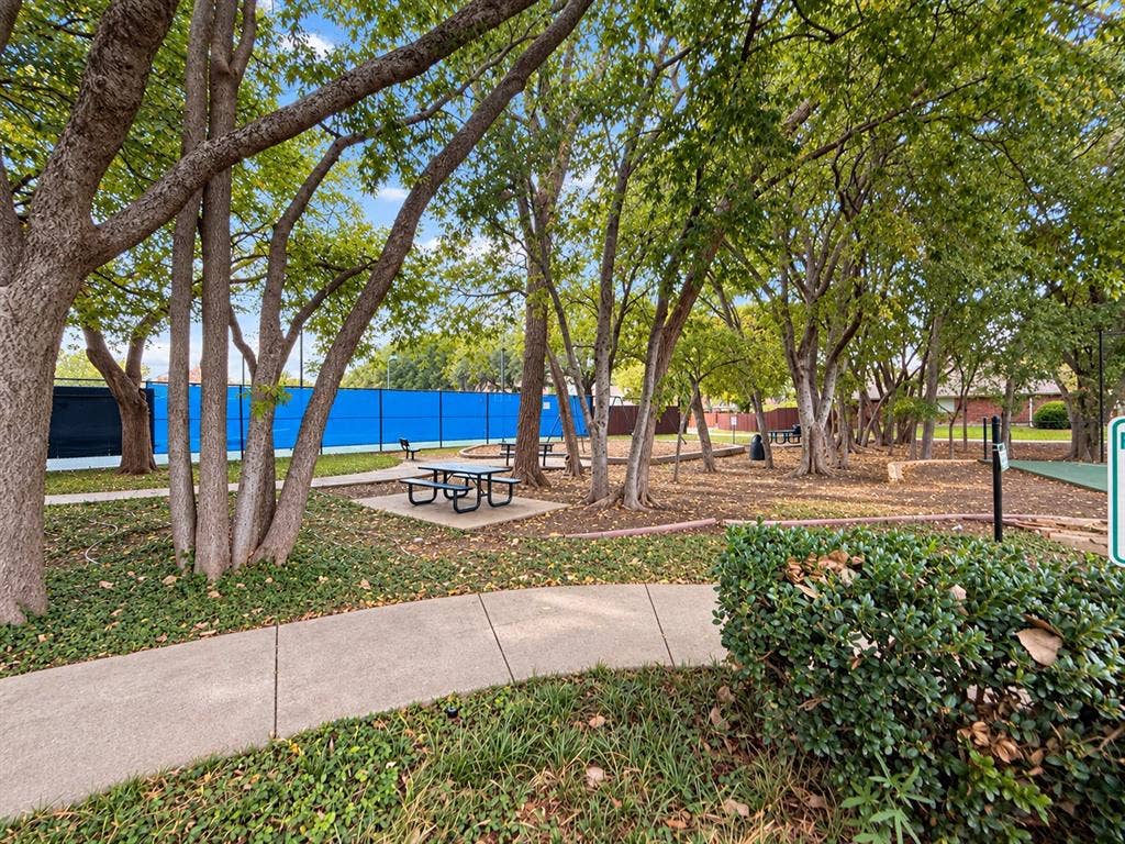 2504 Indian Paint Drive, Plano, TX 75025 Tennis court with blue fencing, paved walking path, picnic tables, mature trees, and landscaped grounds