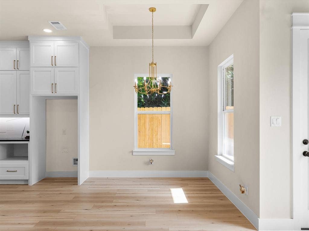 2127 Amanda Avenue, Fort Worth, TX 76105 Recessed ceiling with an ornate chandelier, light wood-finish flooring, white shaker cabinetry, and multiple windows