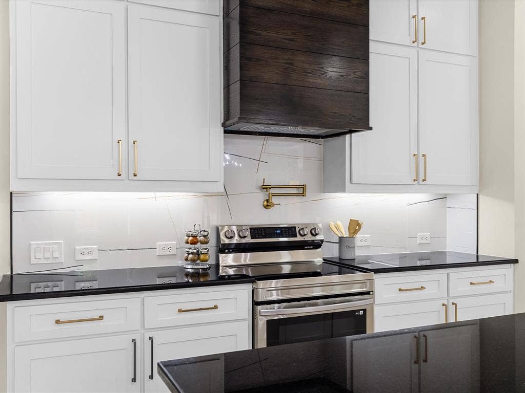 2127 Amanda Avenue, Fort Worth, TX 76105 White shaker cabinetry with gold-tone hardware, dark wood-finish range hood, stainless steel range, pot filler, and black countertops