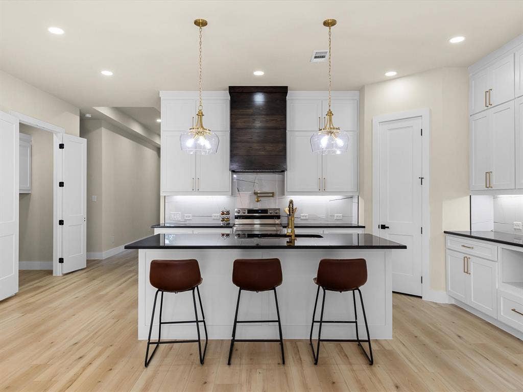2127 Amanda Avenue, Fort Worth, TX 76105 Kitchen featuring an island with black countertop, white shaker cabinetry, gold-tone hardware, wood-finish flooring, and recessed lighting