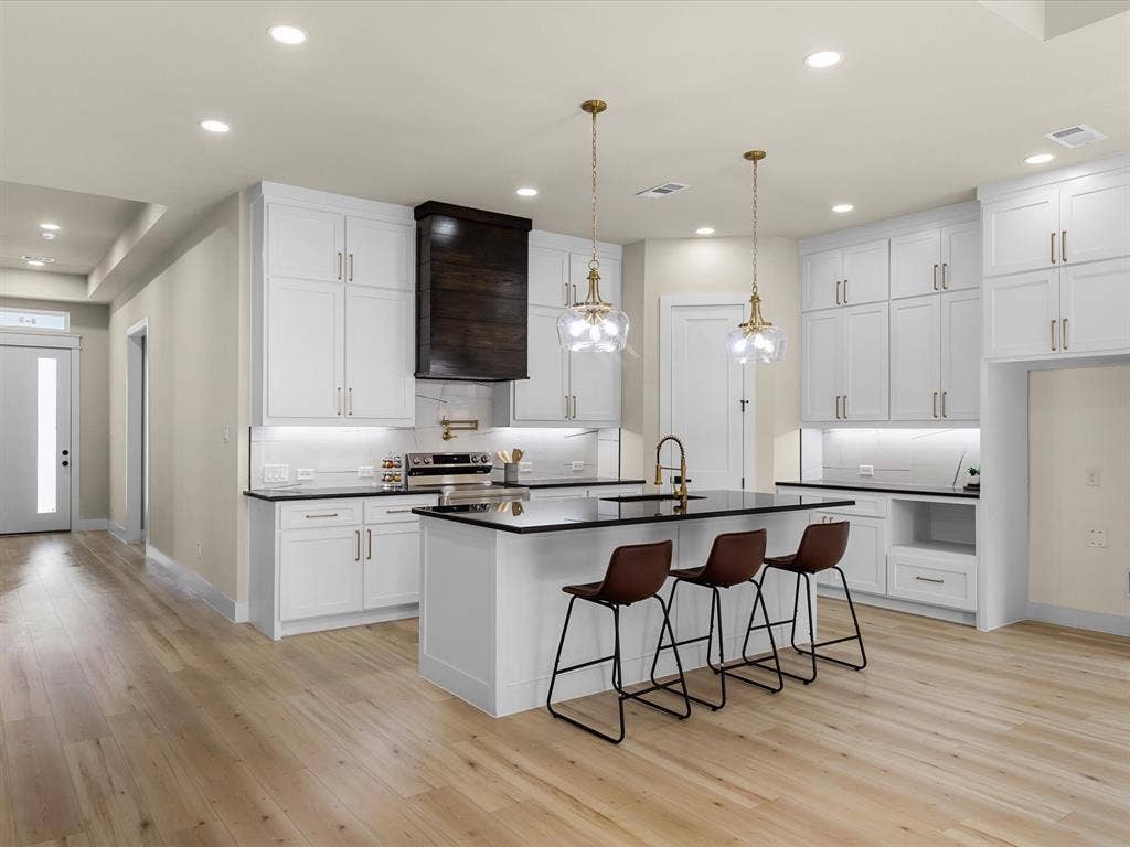 2127 Amanda Avenue, Fort Worth, TX 76105 Kitchen featuring light wood-finish flooring, white cabinetry with gold-tone hardware, dark countertops, and a central island with pendant lighting