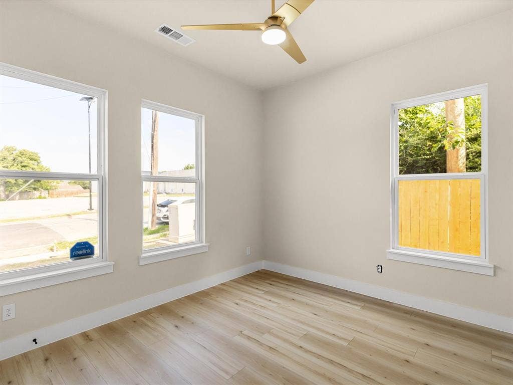 2127 Amanda Avenue, Fort Worth, TX 76105 Light wood-finish flooring, three windows with white trim, a gold-toned ceiling fan, and light-colored walls