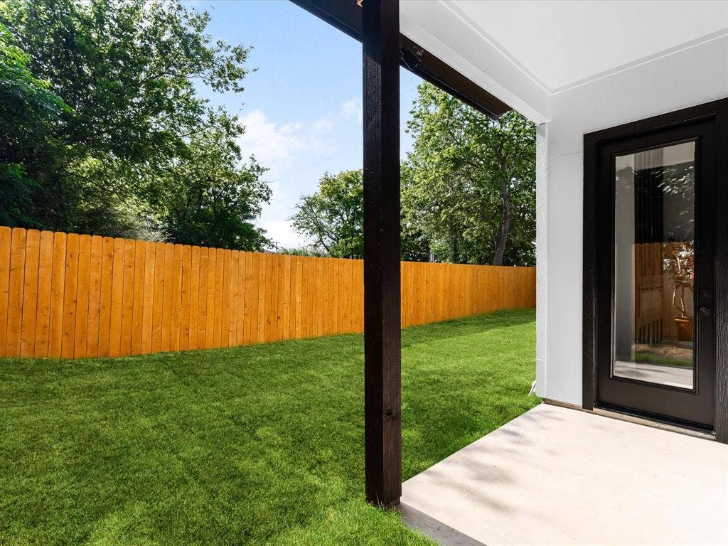 2127 Amanda Avenue, Fort Worth, TX 76105 Expansive grassy yard with a wooden privacy fence, shaded patio, and a dark-framed glass door