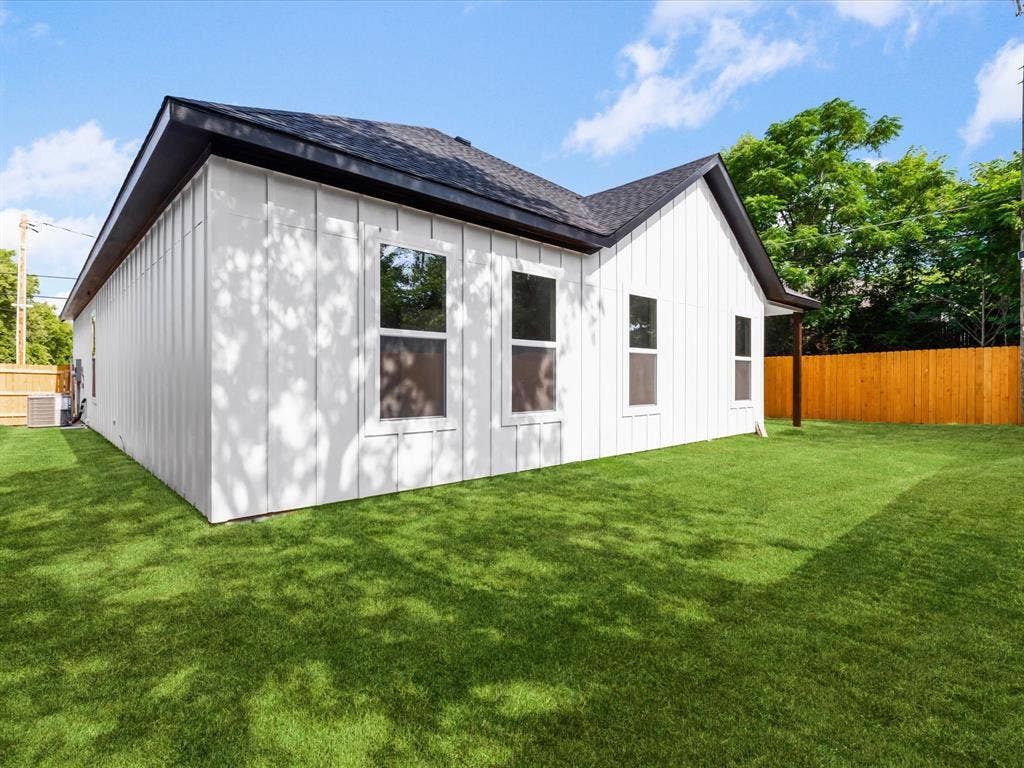2127 Amanda Avenue, Fort Worth, TX 76105 White vertical board siding, black roof shingles, multiple windows, and a wooden privacy fence