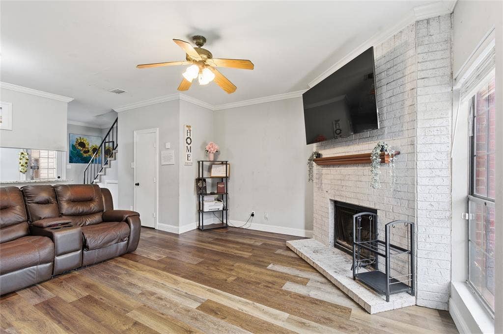 212 Samuel Boulevard, #3, Coppell, TX 75019 Living area featuring wood-finish flooring, a white-painted brick fireplace with a wood mantel, crown molding, and a ceiling fan with light fixture