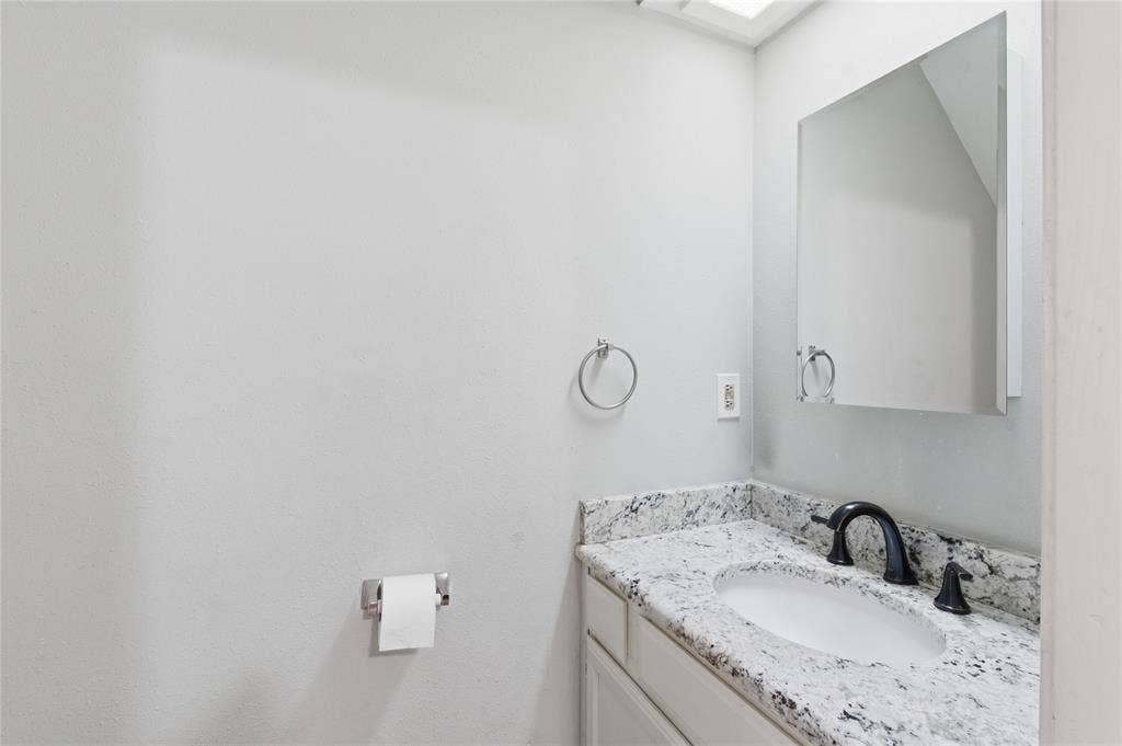 212 Samuel Boulevard, #3, Coppell, TX 75019 White vanity with a speckled countertop, undermount sink, black faucet, and a wall-mounted medicine cabinet