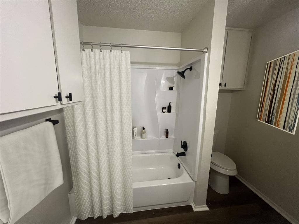 4639 Williams Road, #219, Benbrook, TX 76116 Bathroom featuring a textured ceiling, shower / bath combination with curtain, and wood finished floors