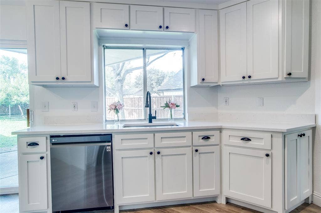 8341 Edgewater Drive, Frisco, TX 75034 White shaker-style cabinetry with black hardware, stainless steel dishwasher, undermount sink with a black gooseneck faucet, and light-toned countertops