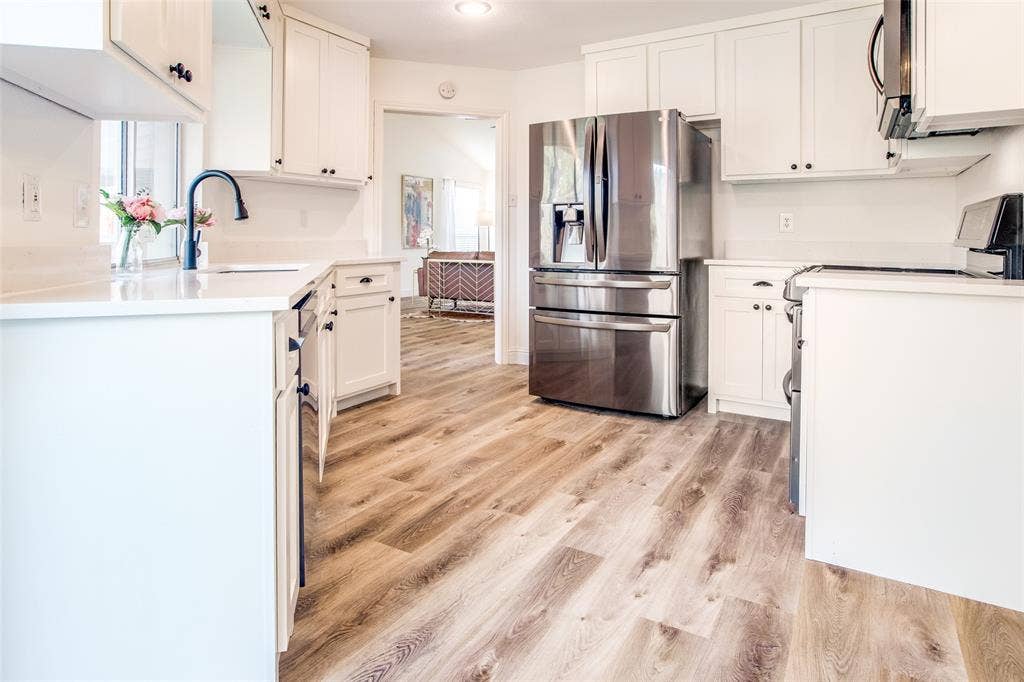 8341 Edgewater Drive, Frisco, TX 75034 White cabinetry, wood-finish flooring, undermount sink with a matte black faucet, stainless steel French door refrigerator, and white countertops