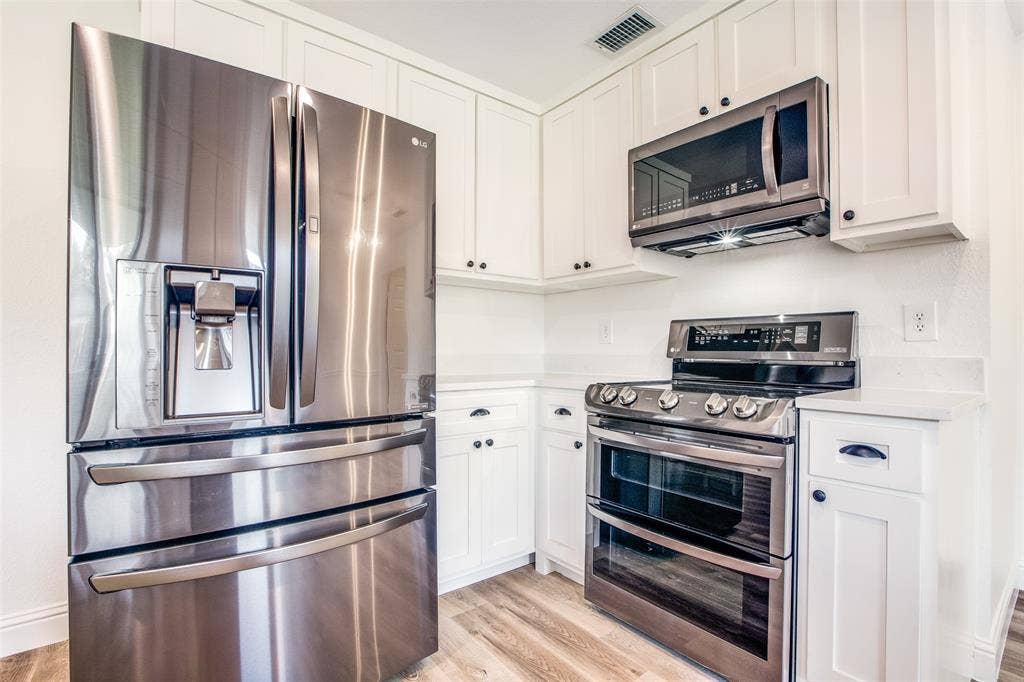 8341 Edgewater Drive, Frisco, TX 75034 Stainless steel appliances, wood-finish flooring, white cabinetry with black hardware, and light-toned countertops