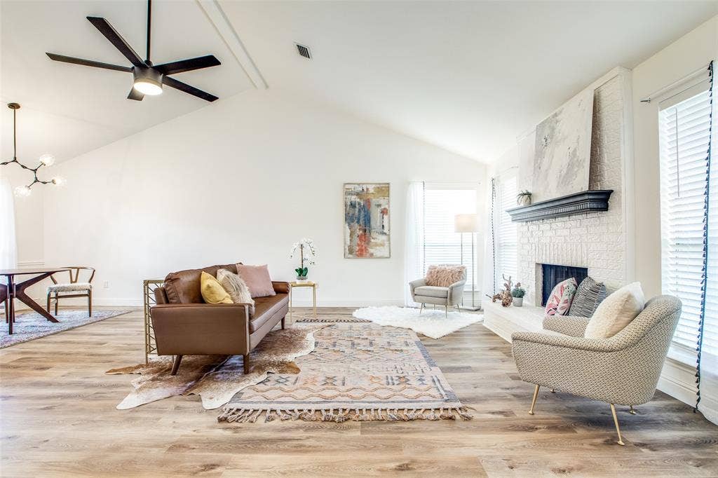 8341 Edgewater Drive, Frisco, TX 75034 Vaulted ceiling with a contemporary ceiling fan, wood-finish flooring, white painted brick fireplace with a dark wood mantel, and multiple windows with blinds