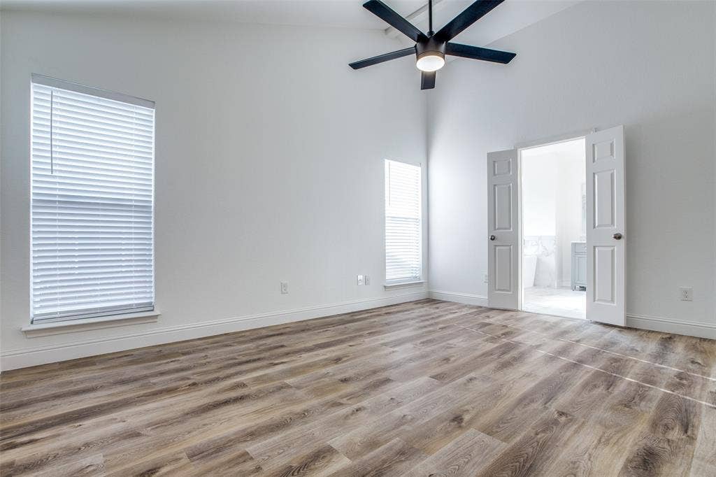 8341 Edgewater Drive, Frisco, TX 75034 Vaulted ceiling with a black ceiling fan, wood-finish flooring, two windows with blinds, and white double doors