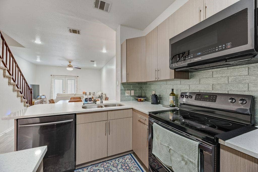 3801 14th Street, #1905, Plano, TX 75074 Contemporary kitchen featuring light wood-finish cabinetry, light-toned countertops, a full suite of black appliances, and a subway tile backsplash