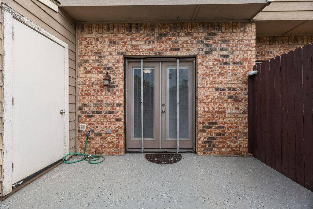3801 14th Street, #1905, Plano, TX 75074 Brick wall exterior featuring double entry doors, an outdoor light fixture, and a privacy fence