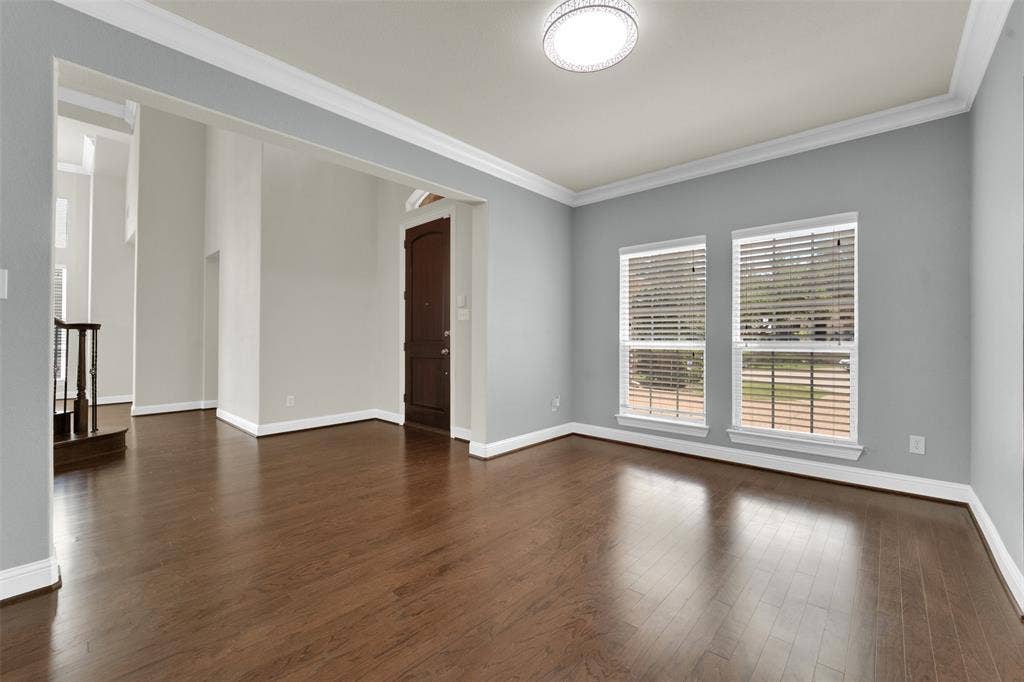 6811 Shady View Court, Sachse, TX 75048 Dark wood-finish flooring, two large windows with blinds, crown molding, and a decorative flush-mount ceiling light