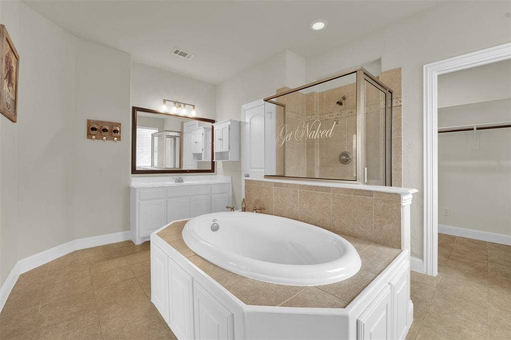 6811 Shady View Court, Sachse, TX 75048 Soaking tub with tiled surround, glass-enclosed shower, single vanity with integrated sink, large wall mirror, and tile flooring