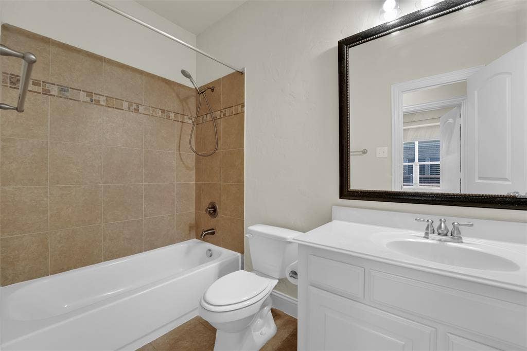 6811 Shady View Court, Sachse, TX 75048 Tiled shower surround with decorative accent band, white bathtub, vanity with integrated sink, chrome fixtures, and framed mirror