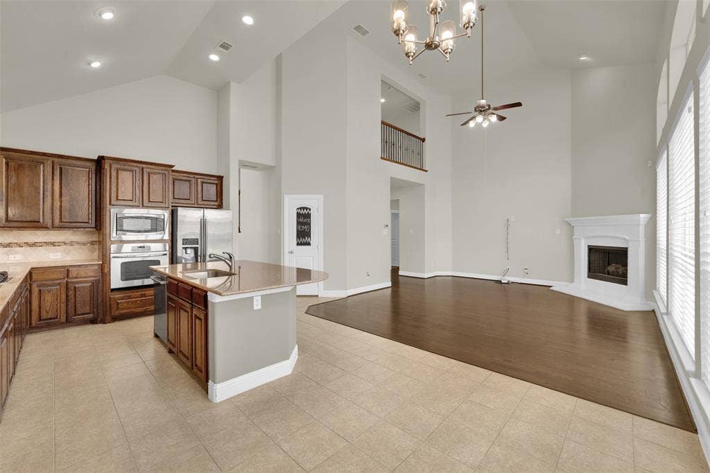 6811 Shady View Court, Sachse, TX 75048 Vaulted ceilings with recessed lighting, wood-finish flooring, a kitchen island with a sink, built-in stainless steel appliances, and a fireplace with a mantel