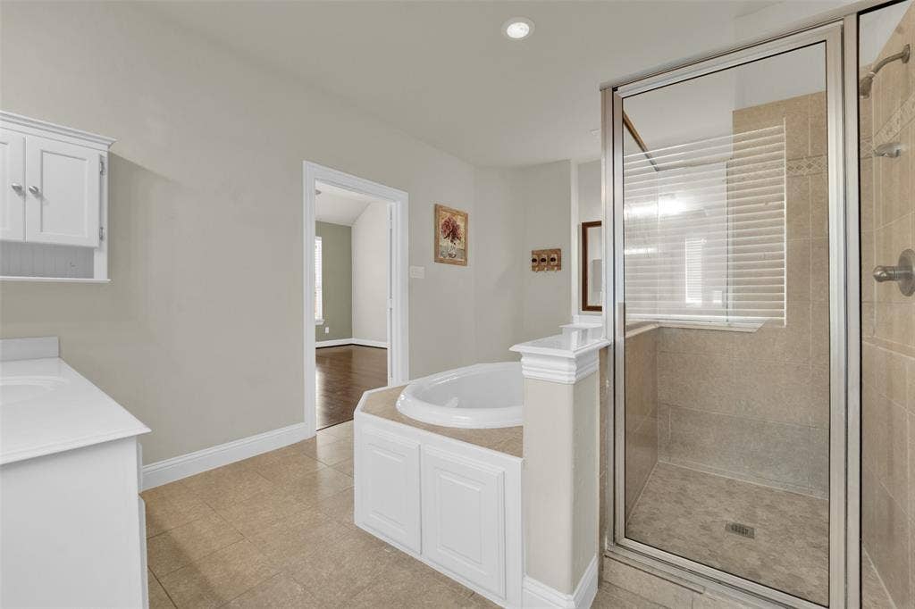 6811 Shady View Court, Sachse, TX 75048 Tiled flooring, white vanity with integrated sink, built-in soaking tub, glass-enclosed shower, and recessed lighting